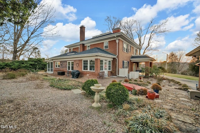 back of property featuring a patio area, a chimney, and brick siding