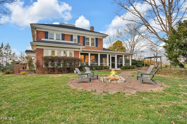 back of house with brick siding, a fire pit, a lawn, a chimney, and a sunroom