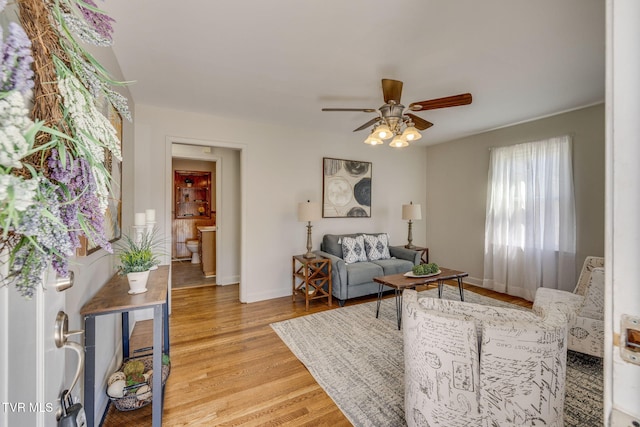 living room featuring a ceiling fan, baseboards, and light wood finished floors