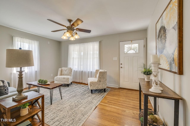 living room with baseboards, light wood-type flooring, and a ceiling fan