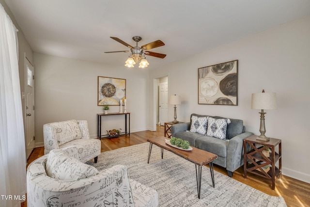 living area with baseboards, wood finished floors, and ceiling fan