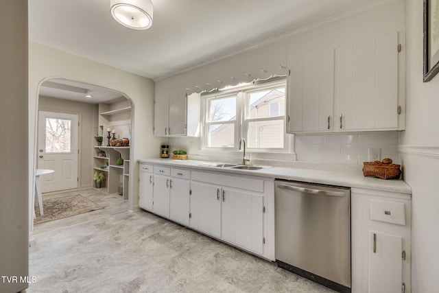 kitchen with arched walkways, a sink, light countertops, white cabinets, and stainless steel dishwasher