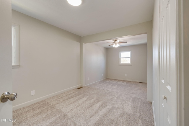 empty room featuring a ceiling fan, light colored carpet, and baseboards