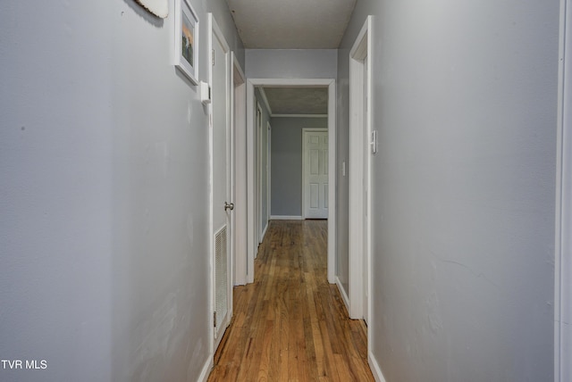 hall featuring visible vents, baseboards, and wood finished floors