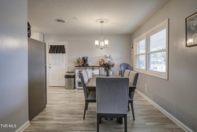 dining space with visible vents, baseboards, light wood-type flooring, and an inviting chandelier