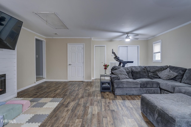 living area featuring wood finished floors, a large fireplace, crown molding, baseboards, and attic access