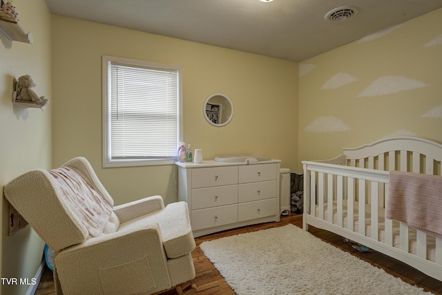 bedroom featuring a nursery area, wood finished floors, and visible vents