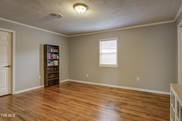 empty room featuring crown molding, wood finished floors, visible vents, and baseboards