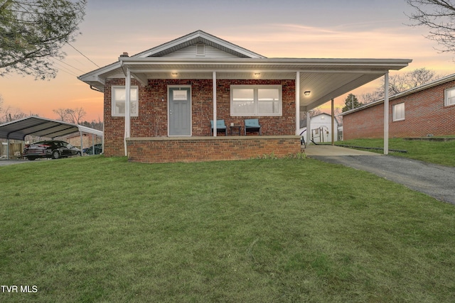 view of front facade with brick siding, aphalt driveway, covered porch, a lawn, and a carport