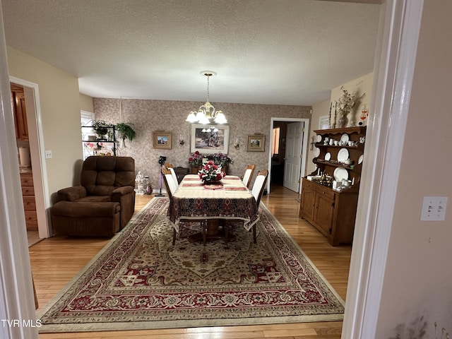 dining space with a textured ceiling, an inviting chandelier, light wood-style flooring, and wallpapered walls