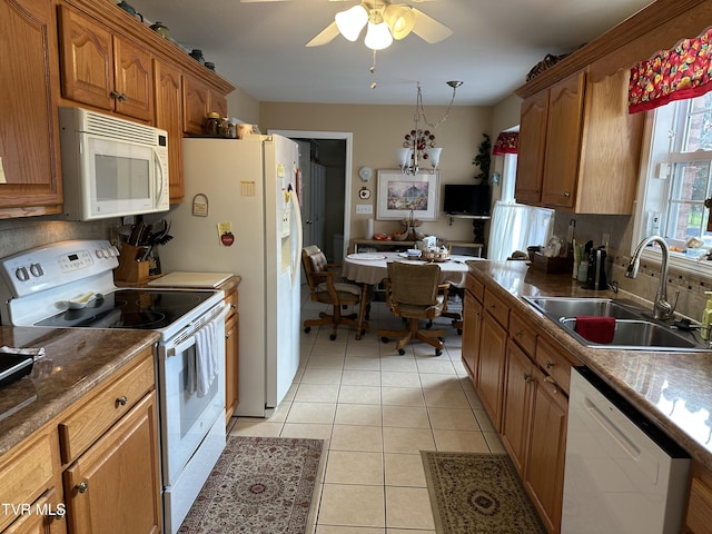 kitchen with light tile patterned floors, brown cabinetry, white appliances, a ceiling fan, and a sink