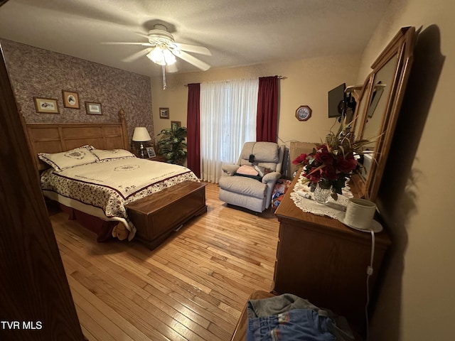 bedroom featuring light wood-style flooring, wallpapered walls, and a ceiling fan