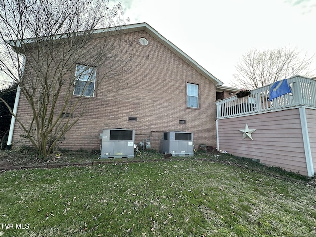 back of property featuring central AC unit, a lawn, and brick siding