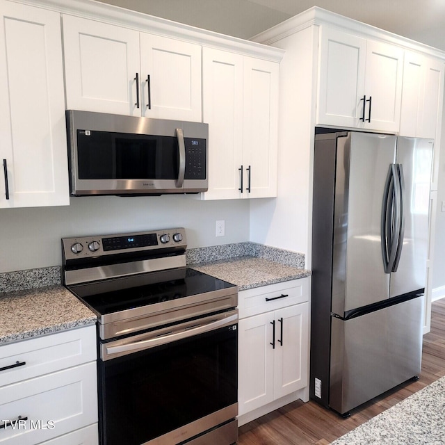 kitchen featuring light stone countertops, white cabinetry, stainless steel appliances, and wood finished floors