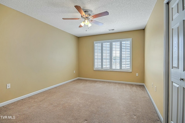 carpeted empty room with visible vents, a textured ceiling, baseboards, and ceiling fan