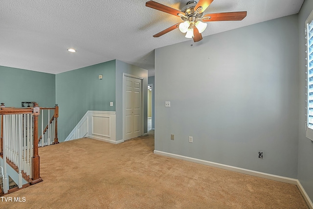 unfurnished room with a textured ceiling, carpet, baseboards, and ceiling fan