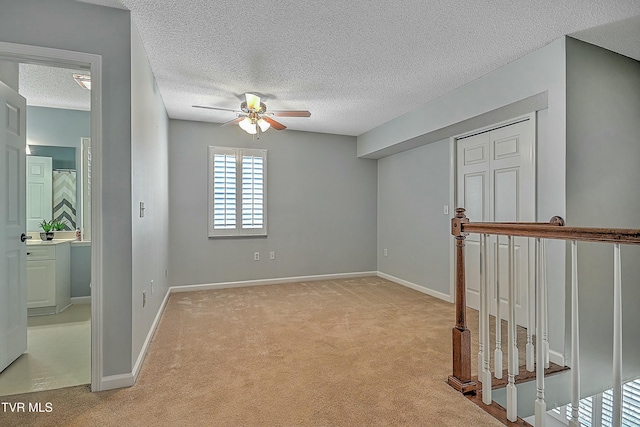 spare room with baseboards, a ceiling fan, light colored carpet, and a textured ceiling