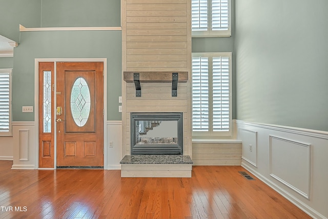 foyer featuring hardwood / wood-style floors, visible vents, a multi sided fireplace, and wainscoting