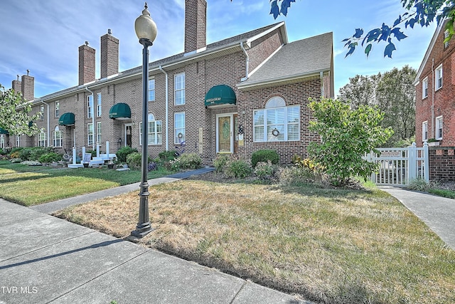 view of front of home with brick siding, a chimney, and a front yard