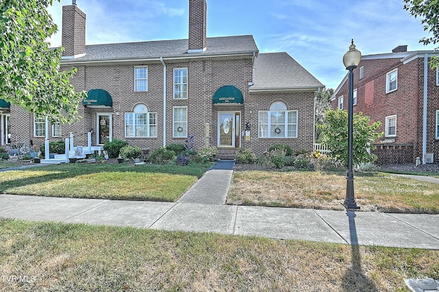 view of front of property featuring brick siding, a chimney, and a front lawn