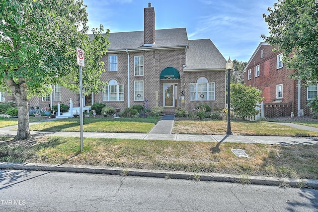 view of front facade with brick siding, a chimney, and a front yard