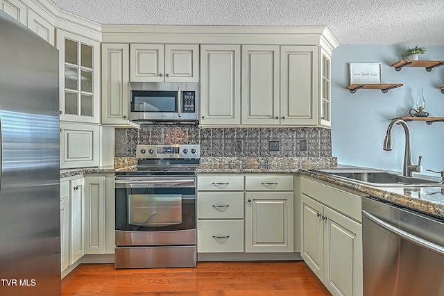 kitchen featuring wood finished floors, a sink, decorative backsplash, stainless steel appliances, and a textured ceiling