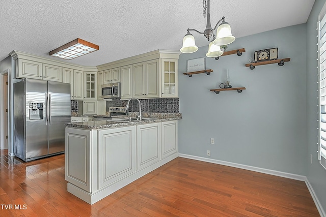 kitchen featuring wood finished floors, dark stone counters, appliances with stainless steel finishes, a peninsula, and an inviting chandelier