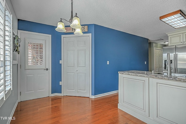 kitchen featuring a chandelier, a textured ceiling, light wood-style floors, and stainless steel refrigerator with ice dispenser