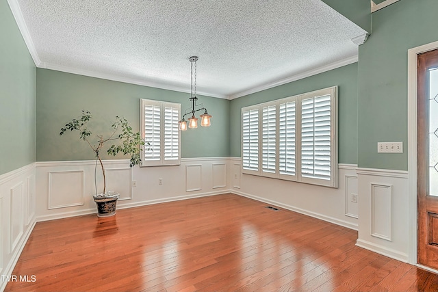 unfurnished dining area featuring hardwood / wood-style flooring, crown molding, and a wainscoted wall