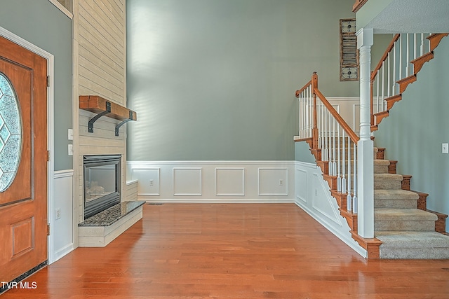 foyer entrance featuring stairway, wainscoting, a fireplace, and wood finished floors