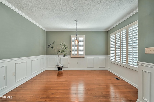 unfurnished dining area featuring hardwood / wood-style flooring, crown molding, visible vents, and a textured ceiling