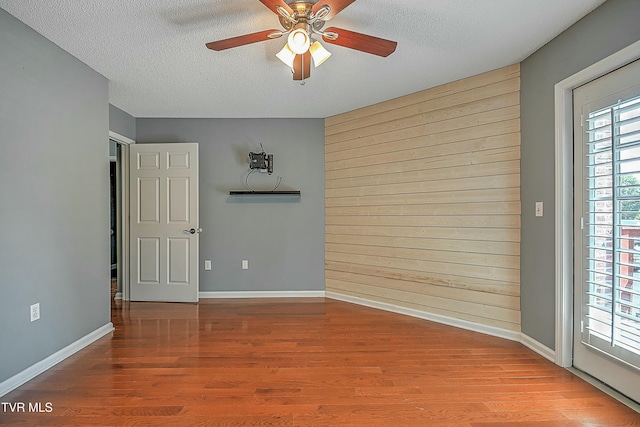 spare room with wood walls, a textured ceiling, a ceiling fan, and wood finished floors