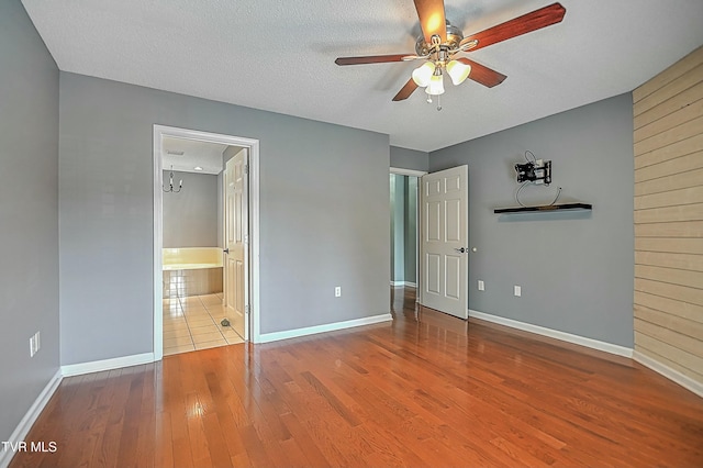 unfurnished bedroom with a textured ceiling, ensuite bathroom, baseboards, and wood finished floors