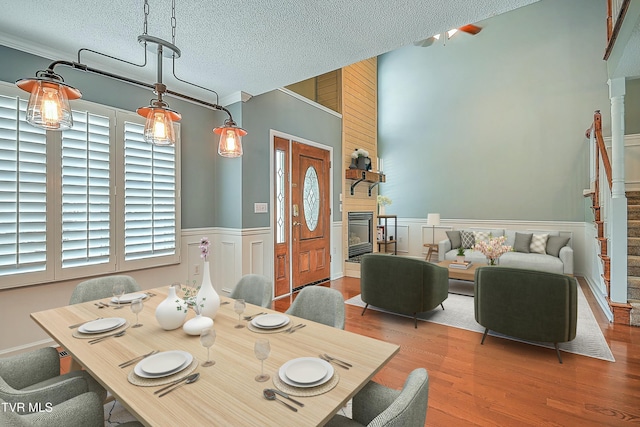 dining area with a textured ceiling, wood finished floors, a fireplace, and wainscoting