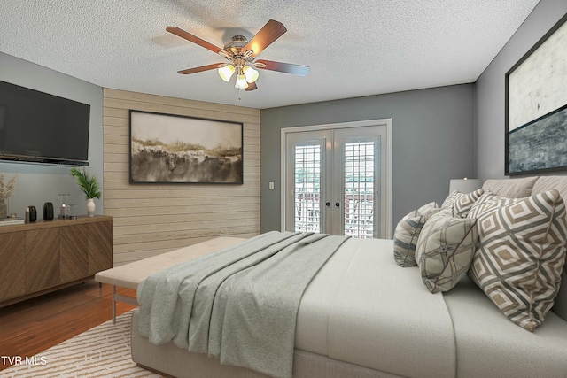 bedroom with access to exterior, wooden walls, french doors, a textured ceiling, and a ceiling fan