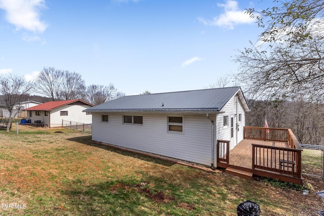 rear view of property with metal roof, a lawn, a wooden deck, and fence