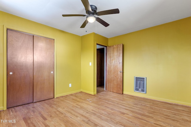 unfurnished bedroom with ceiling fan, baseboards, a closet, light wood-style floors, and heating unit