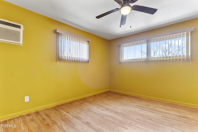 empty room featuring a wealth of natural light, baseboards, wood finished floors, and a wall mounted air conditioner