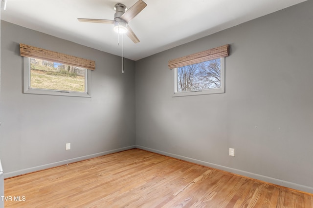 spare room with a wealth of natural light, light wood-style flooring, baseboards, and a ceiling fan