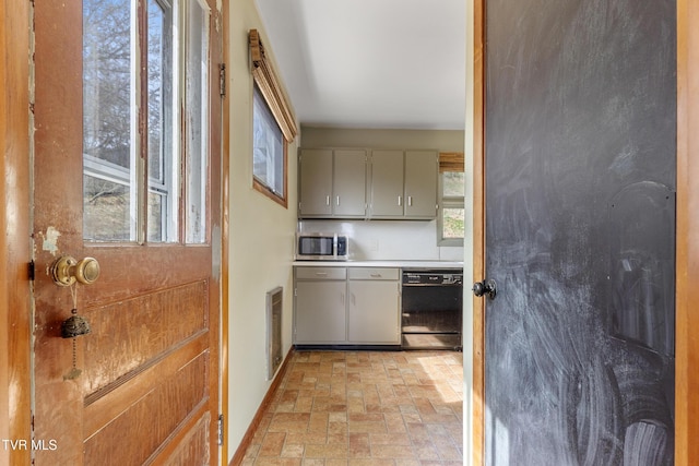 kitchen with gray cabinetry, stainless steel microwave, black dishwasher, brick floor, and baseboards