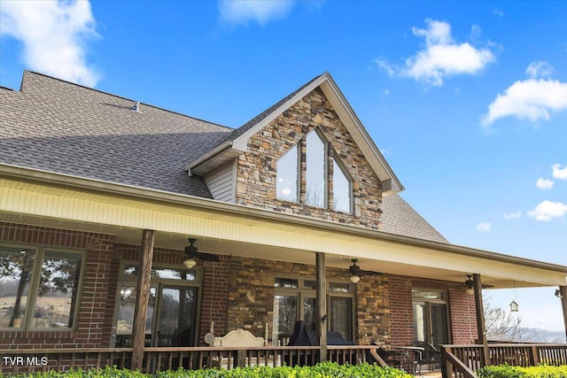 rear view of property featuring brick siding, a ceiling fan, stone siding, and a shingled roof