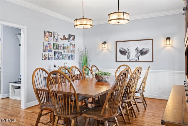 dining room with light wood-type flooring, wainscoting, crown molding, and a decorative wall