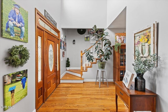 entryway with stairway, baseboards, light wood-style flooring, and a towering ceiling