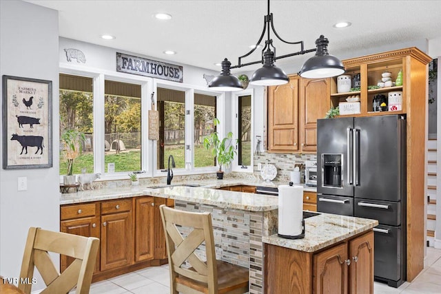 kitchen with brown cabinets, a sink, light stone counters, light tile patterned flooring, and high end black fridge