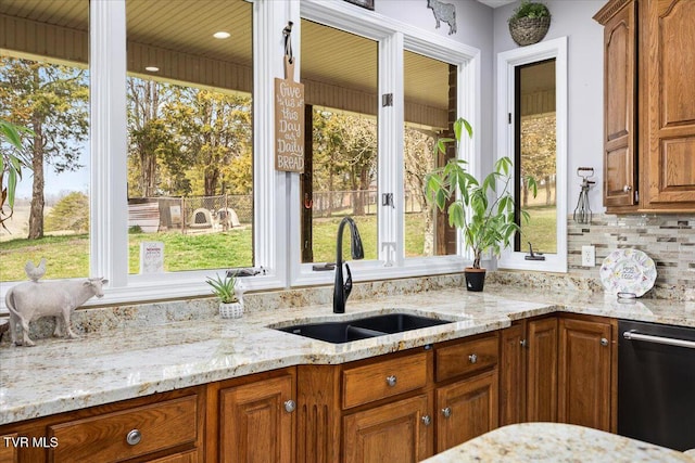 kitchen featuring brown cabinetry, light stone countertops, a sink, dishwasher, and tasteful backsplash