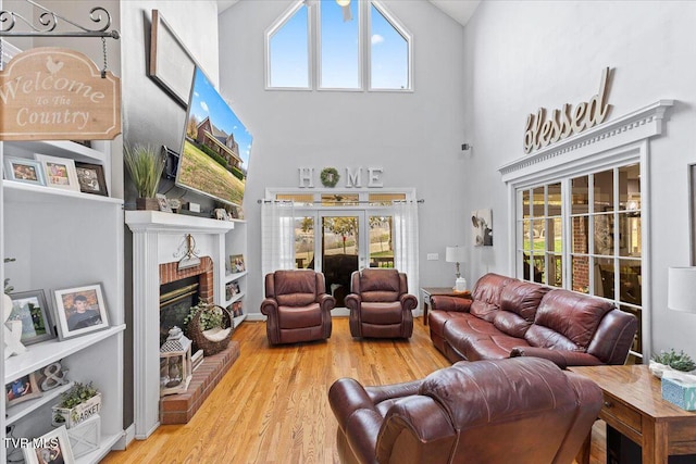 living area featuring a wealth of natural light, a brick fireplace, wood finished floors, and a towering ceiling