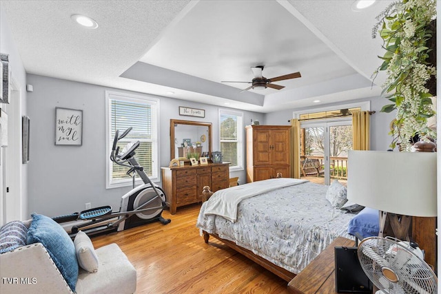 bedroom with light wood finished floors, a tray ceiling, recessed lighting, access to exterior, and a textured ceiling