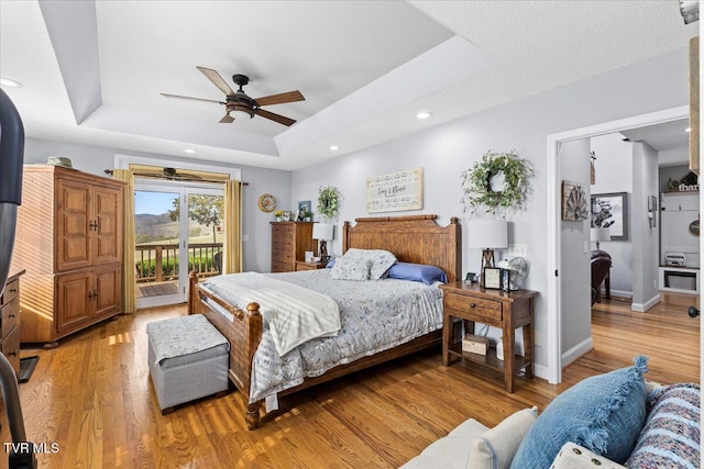 bedroom with baseboards, a raised ceiling, light wood-style flooring, and access to outside