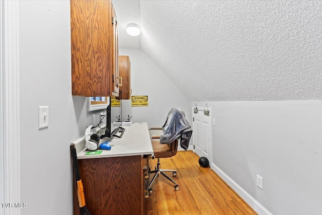 home office with baseboards, a textured ceiling, lofted ceiling, and light wood-style floors