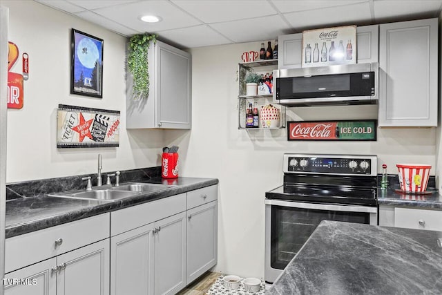 kitchen with dark countertops, appliances with stainless steel finishes, a paneled ceiling, and a sink